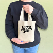Alpha Epsilon Phi tote bag held by a sorority woman, featuring the AEPhi letters in a vibrant design.
