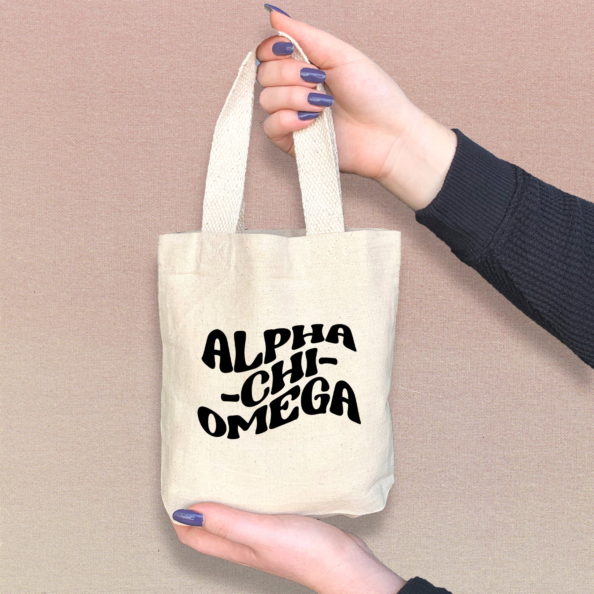 Alpha Chi Omega woman holding a stylish mini tote bag with bold Greek letters printed on the front.