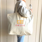 Chi Omega tote bag with layered 3D Greek letters, worn over the shoulder by a woman headed to class.