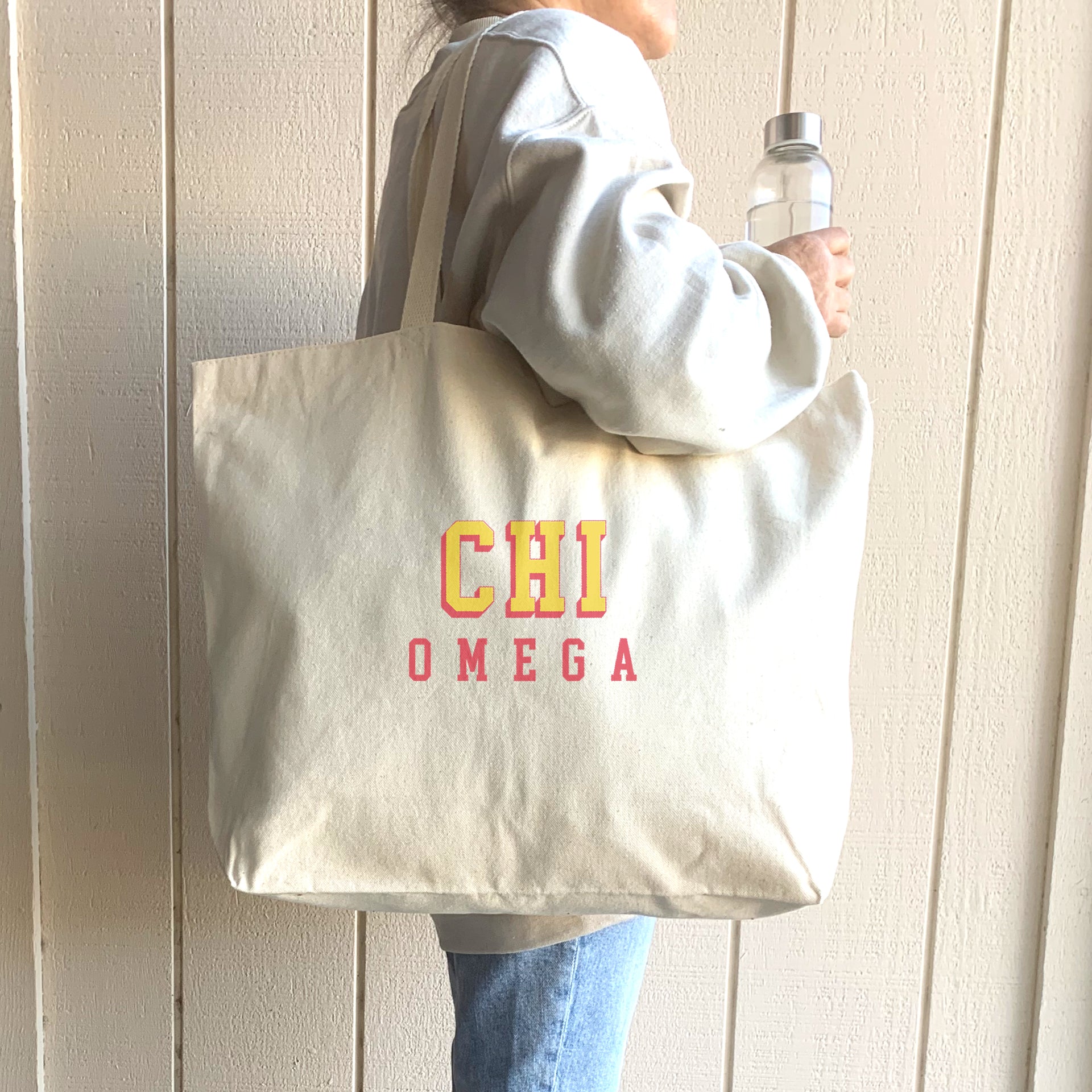 Chi Omega tote bag with layered 3D Greek letters, worn over the shoulder by a woman headed to class.