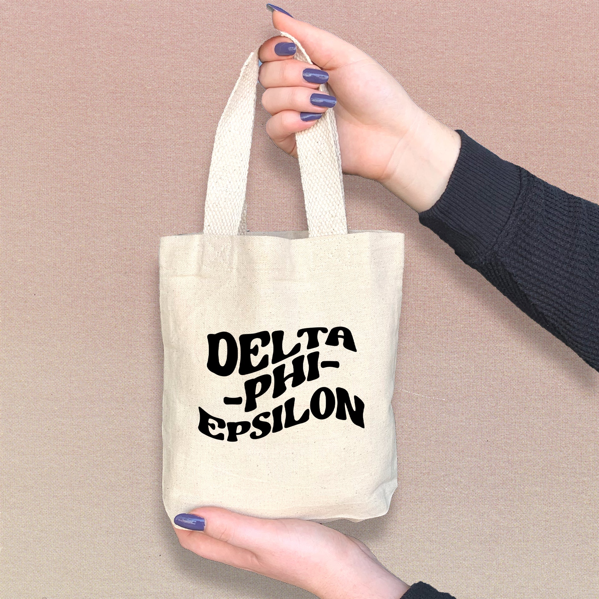 Delta Phi Epsilon sorority woman holding a mini tote bag with Delta Phi Epsilon’s classic letters.