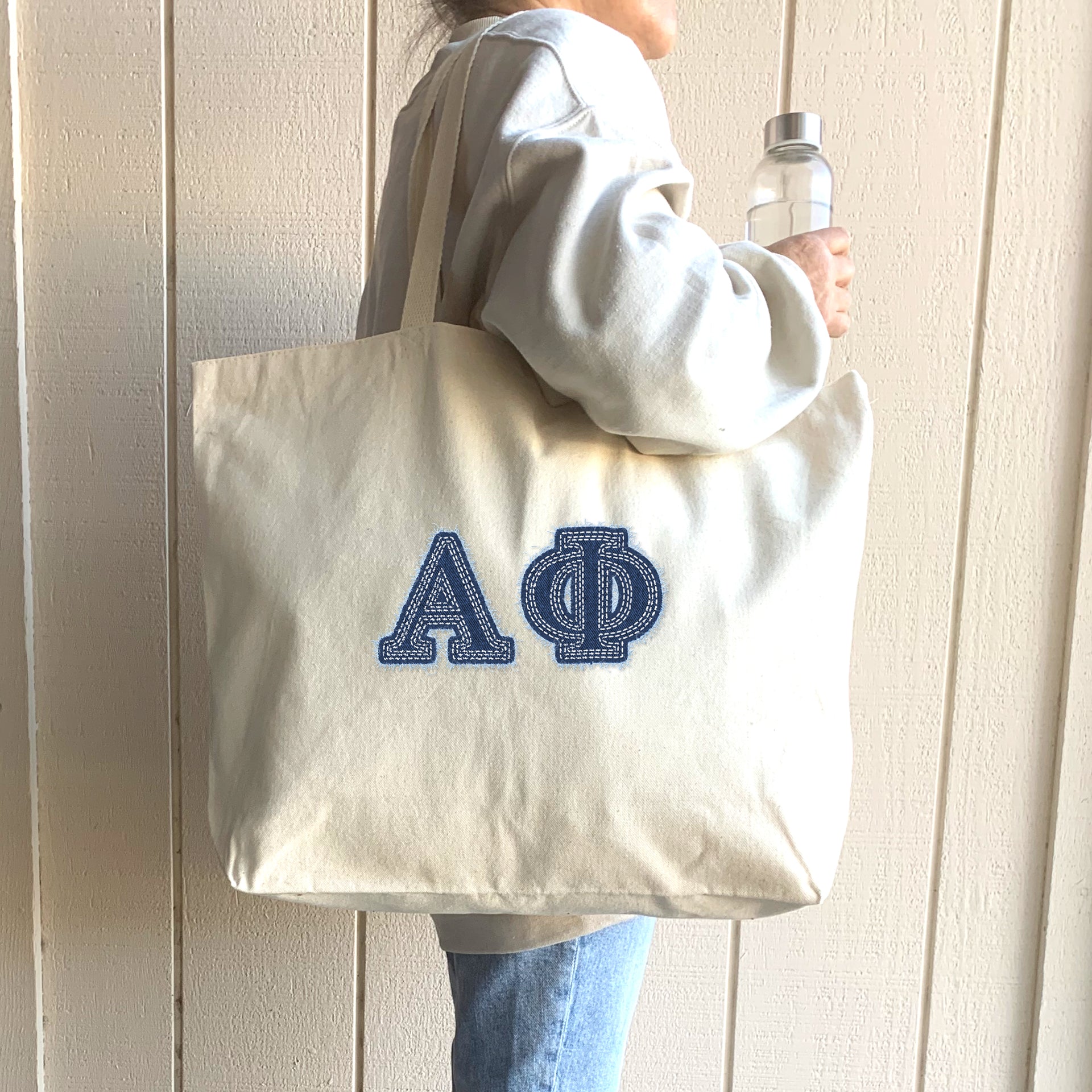 Woman stands outdoors with her Alpha Phi denim tote bag in hand.