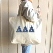 A student carrying a tote bag with denim Delta Delta Delta letters walks confidently to class.