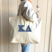 A bright and energetic woman holds her tote with denim Kappa Delta letters while hanging out with her sisters.