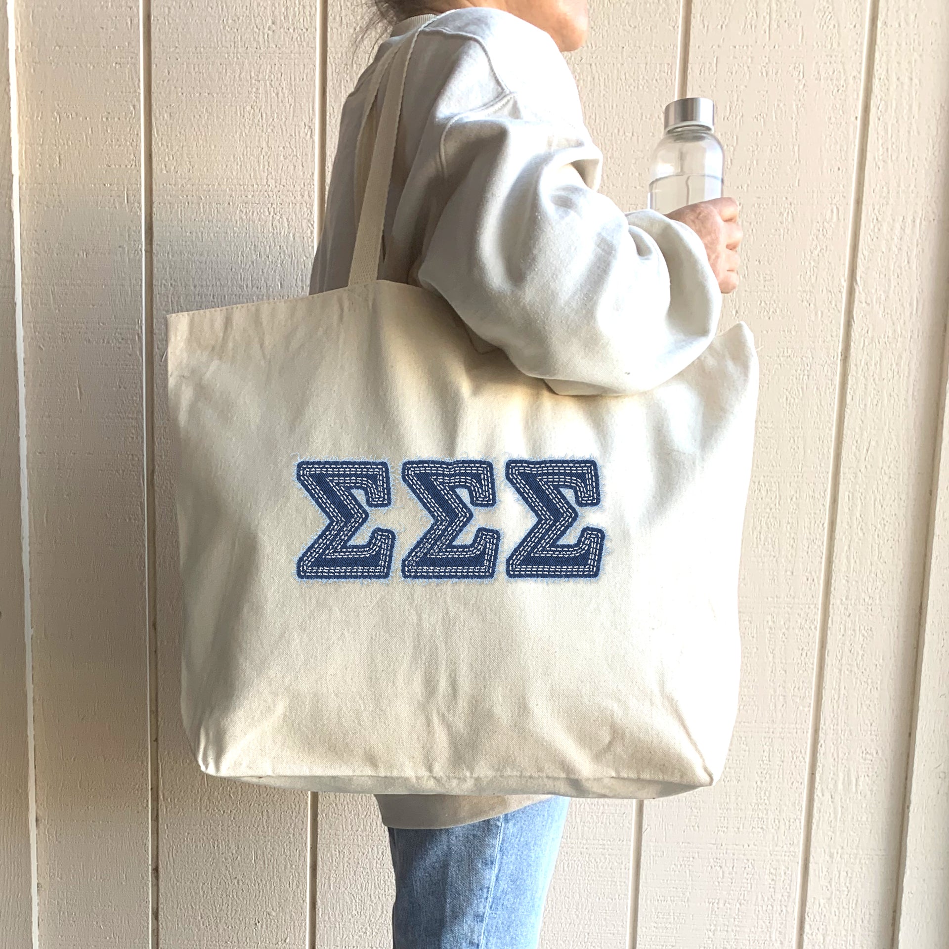 A student smiles with pride as she carries her Sigma Sigma Sigma tote featuring eye-catching denim letters.