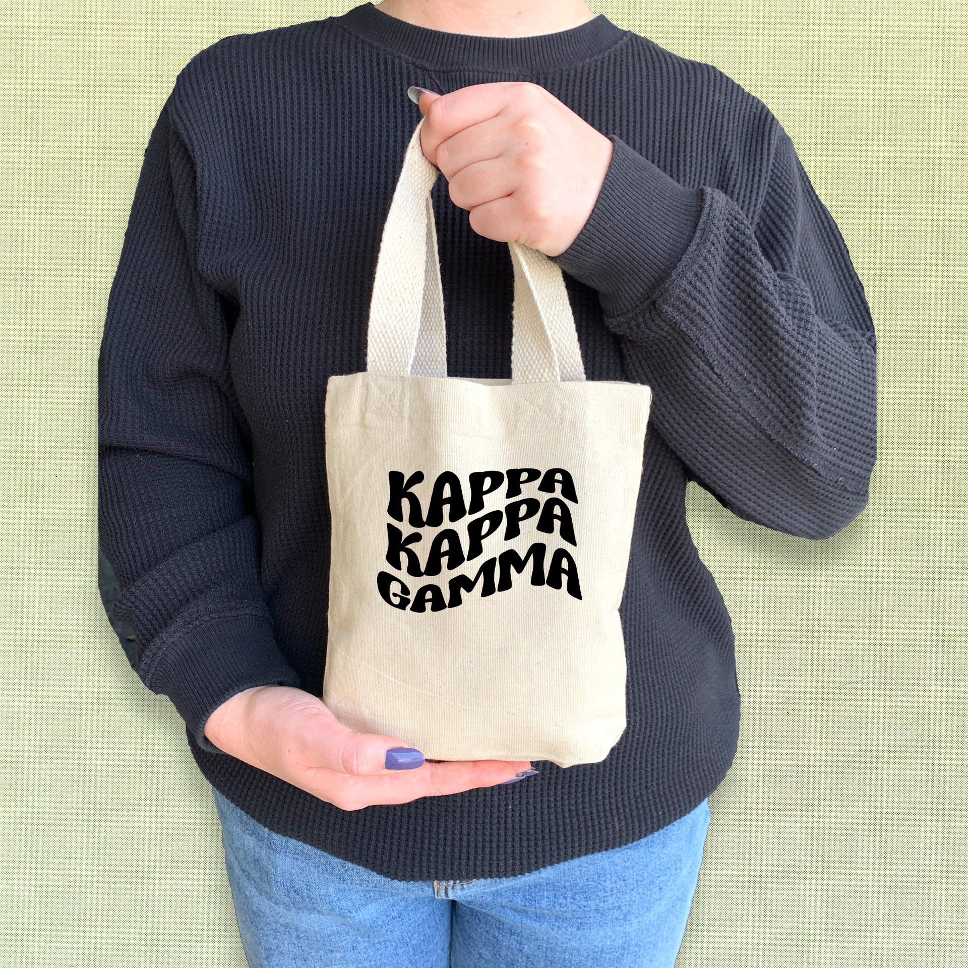 Kappa Kappa Gamma member showing off a mini tote bag printed with bold KKG letters.