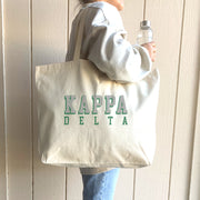 Kappa Delta sorority tote with 3D text, worn over the shoulder of a Kappa Delta member on campus.