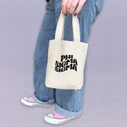 Phi Sigma Sigma woman holding a PSS mini tote bag with clean, classic letter styling.