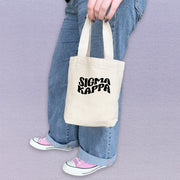 Sigma Kappa sorority woman showing off a compact tote bag printed with Sigma Kappa letters.