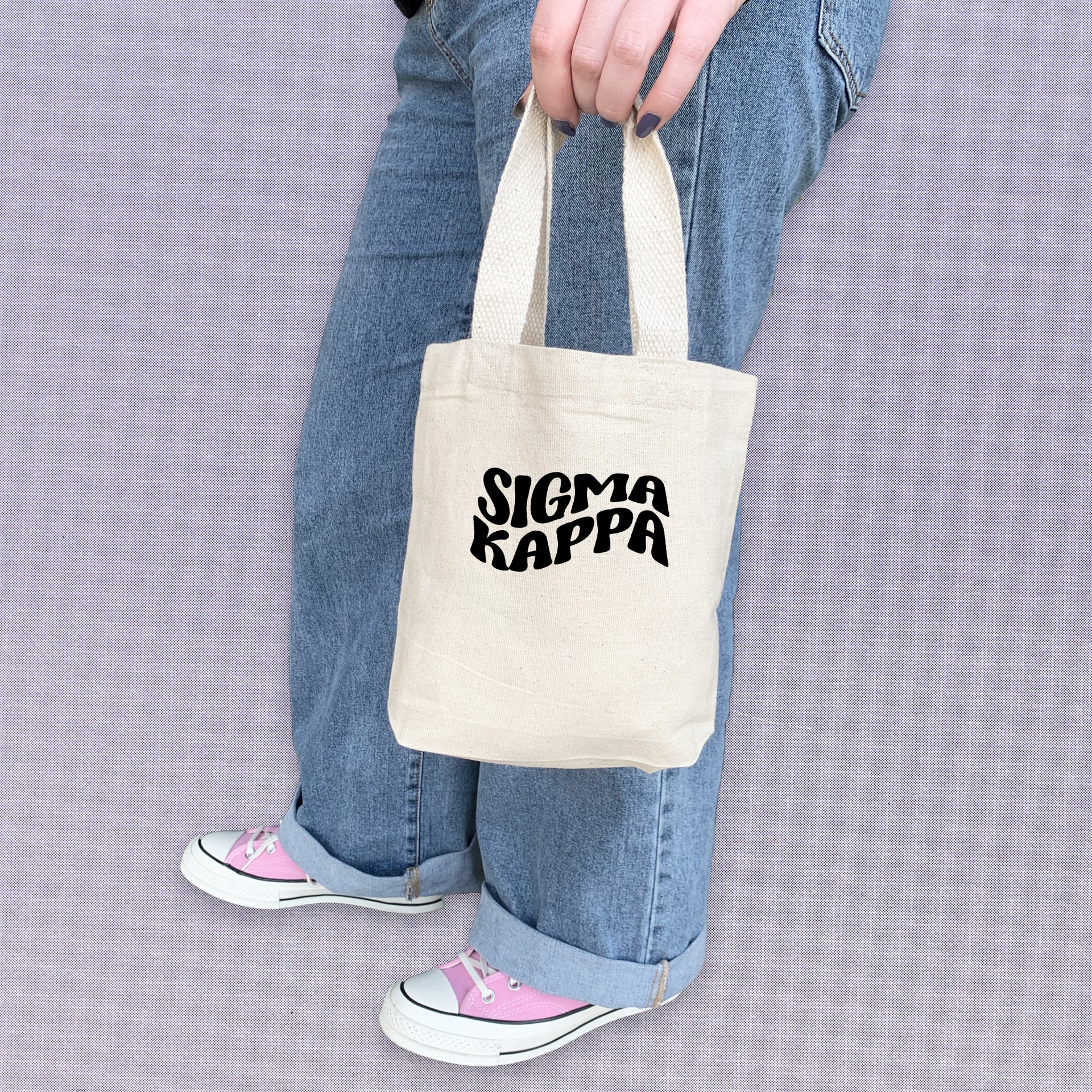 Sigma Kappa sorority woman showing off a compact tote bag printed with Sigma Kappa letters.