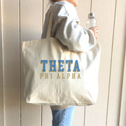 Theta Phi Alpha sorority tote with bold raised text, slung over the shoulder by a member smiling for the camera.