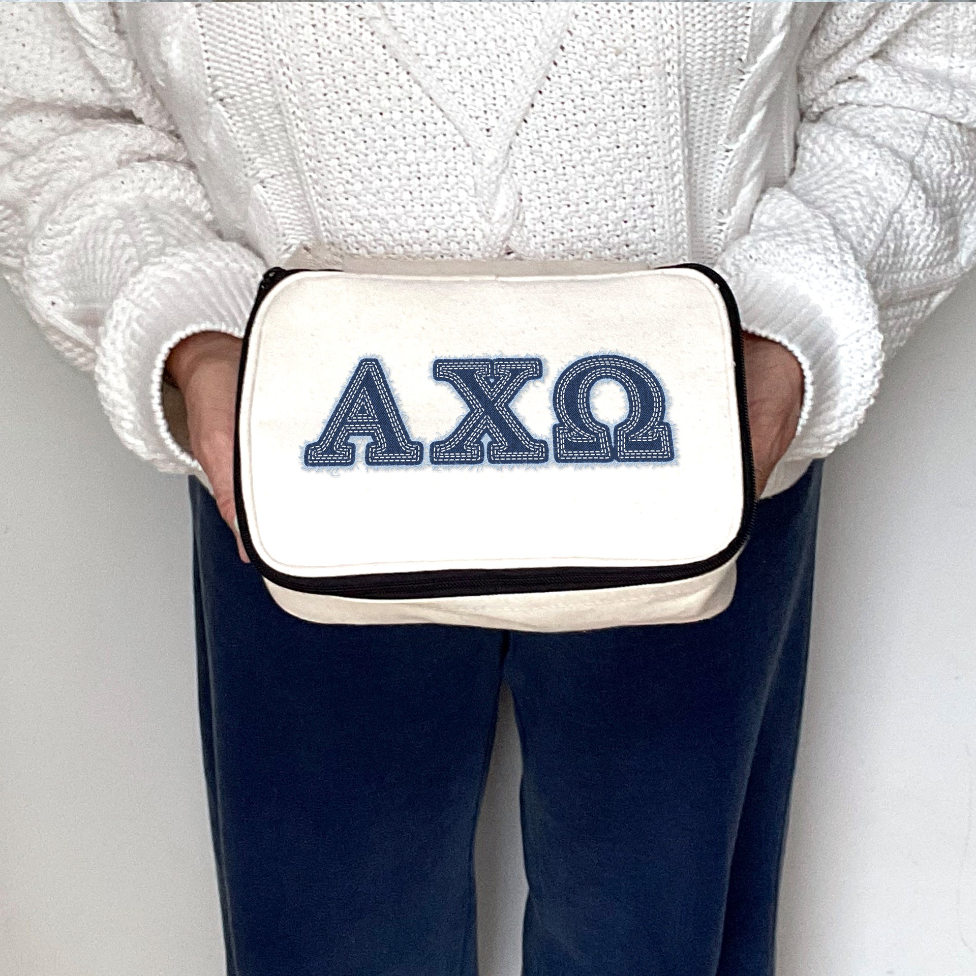 Alpha Chi Omega cosmetic bag held by a sorority member, featuring denim-style Greek letters on canvas.