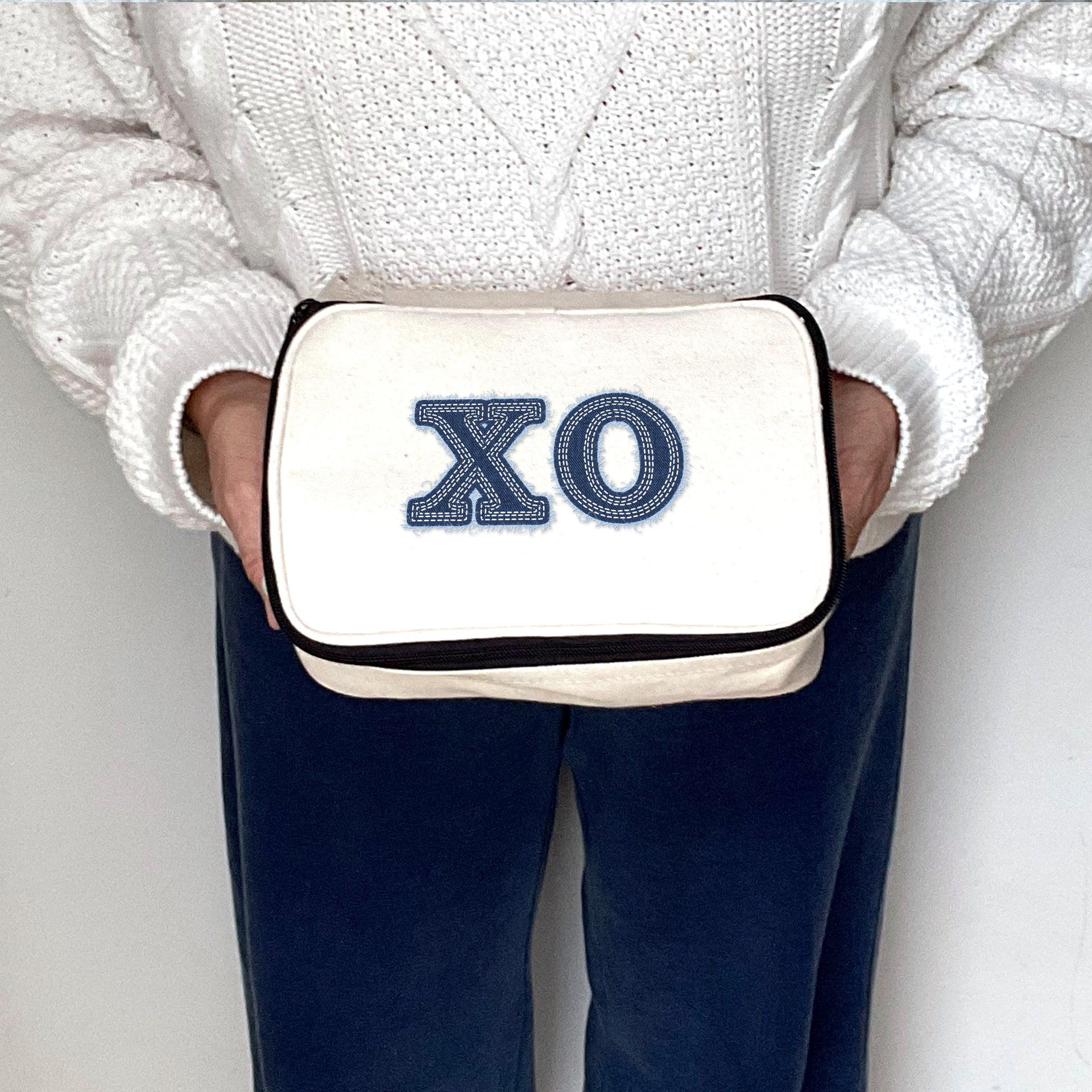 Chi Omega canvas makeup bag with Chi Omega denim-style Greek letters, held for product display.