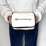 Alpha Omicron Pi cosmetic bag in script lettering held by a woman, shown mid-frame from shoulders to thighs.
