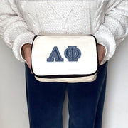 Alpha Phi sorority member holding a cosmetic pouch printed with Alpha Phi denim-style Greek letters.
