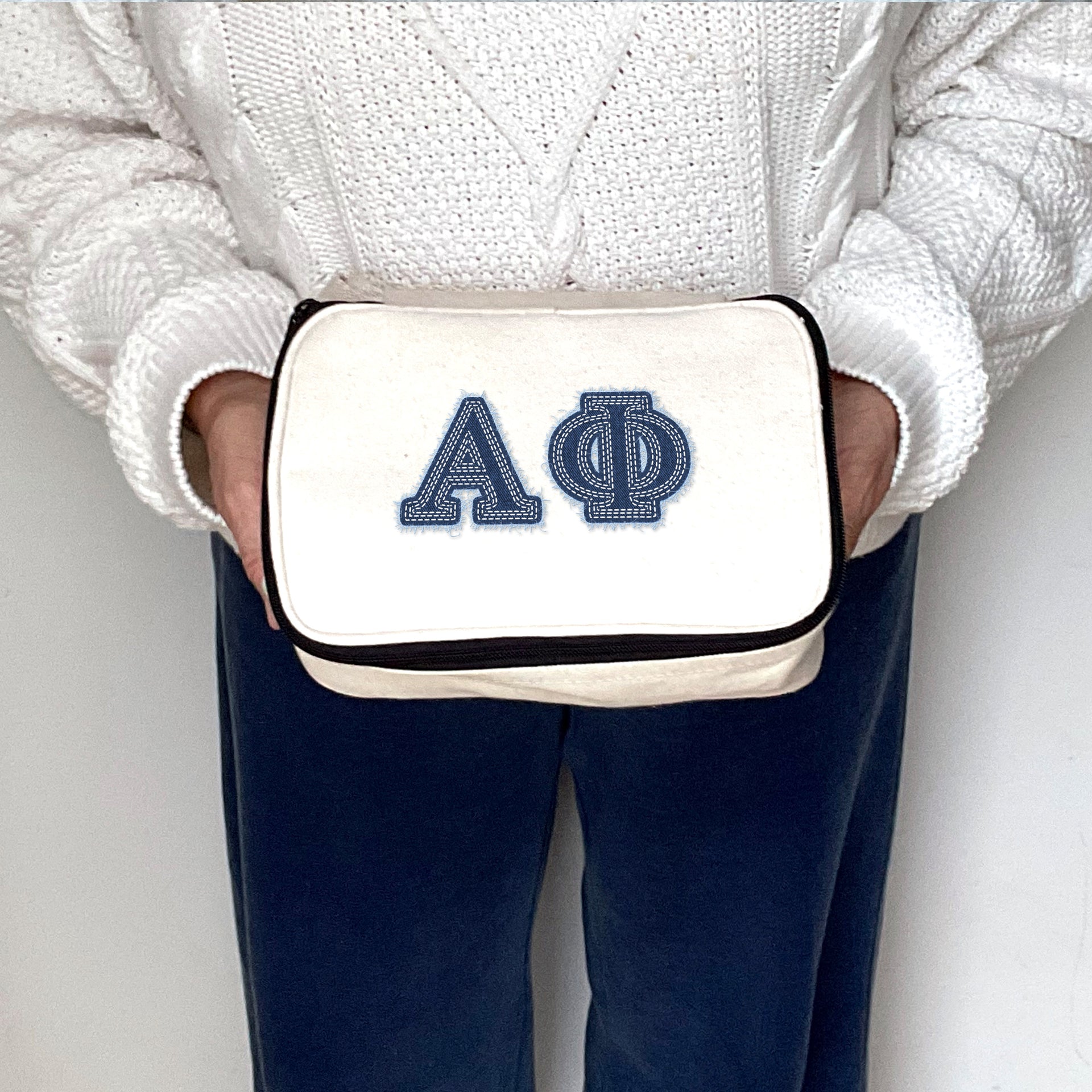 Alpha Phi sorority member holding a cosmetic pouch printed with Alpha Phi denim-style Greek letters.