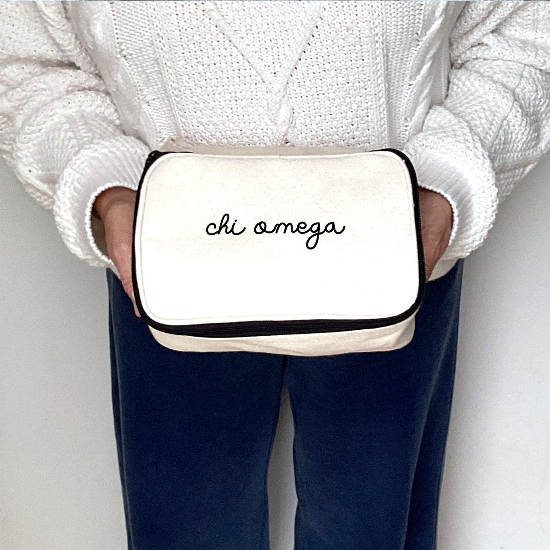 Mid-frame photo of a woman holding a Chi Omega makeup bag with elegant script lettering across the top.