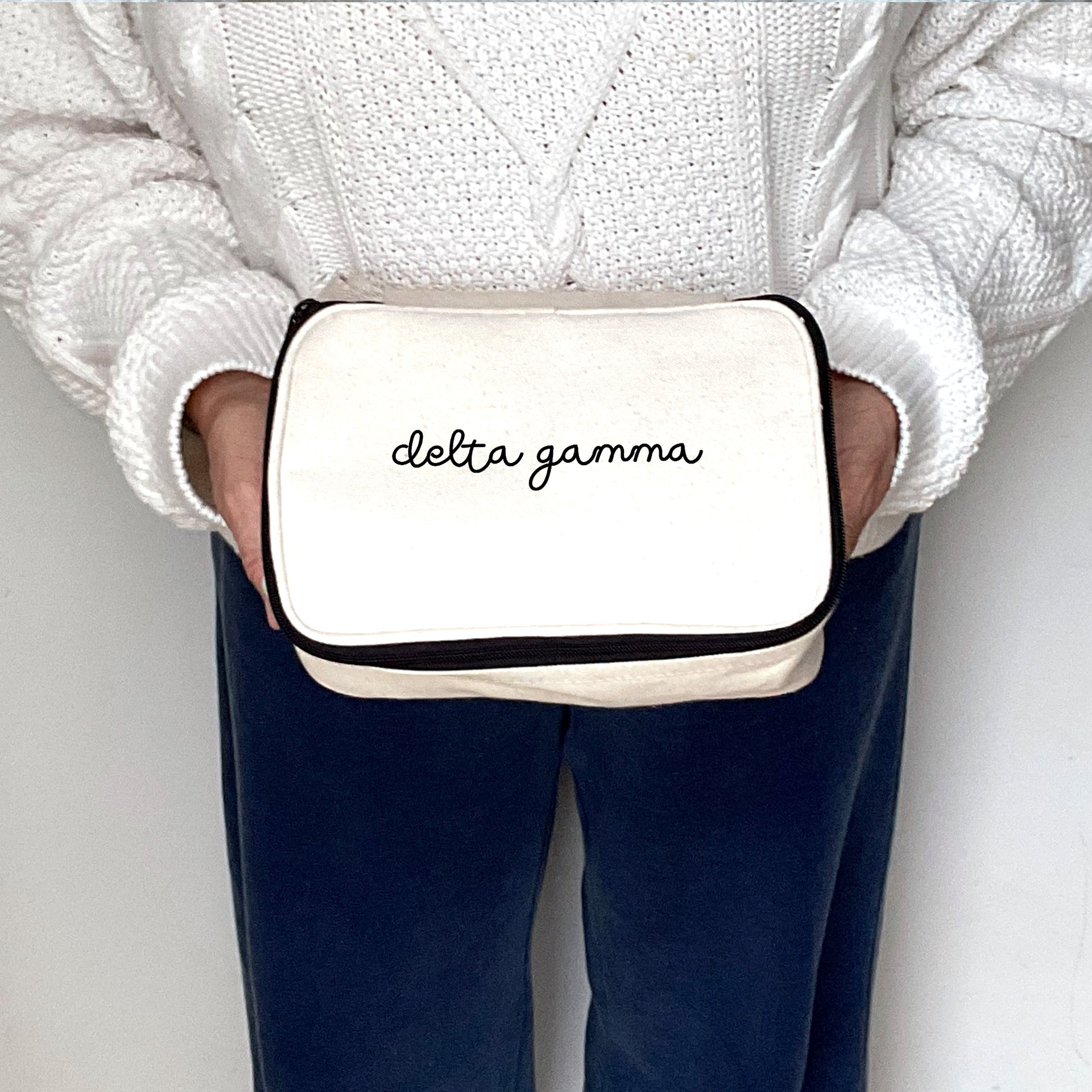 Canvas Delta Gamma makeup bag held by a model photographed shoulder to thigh.