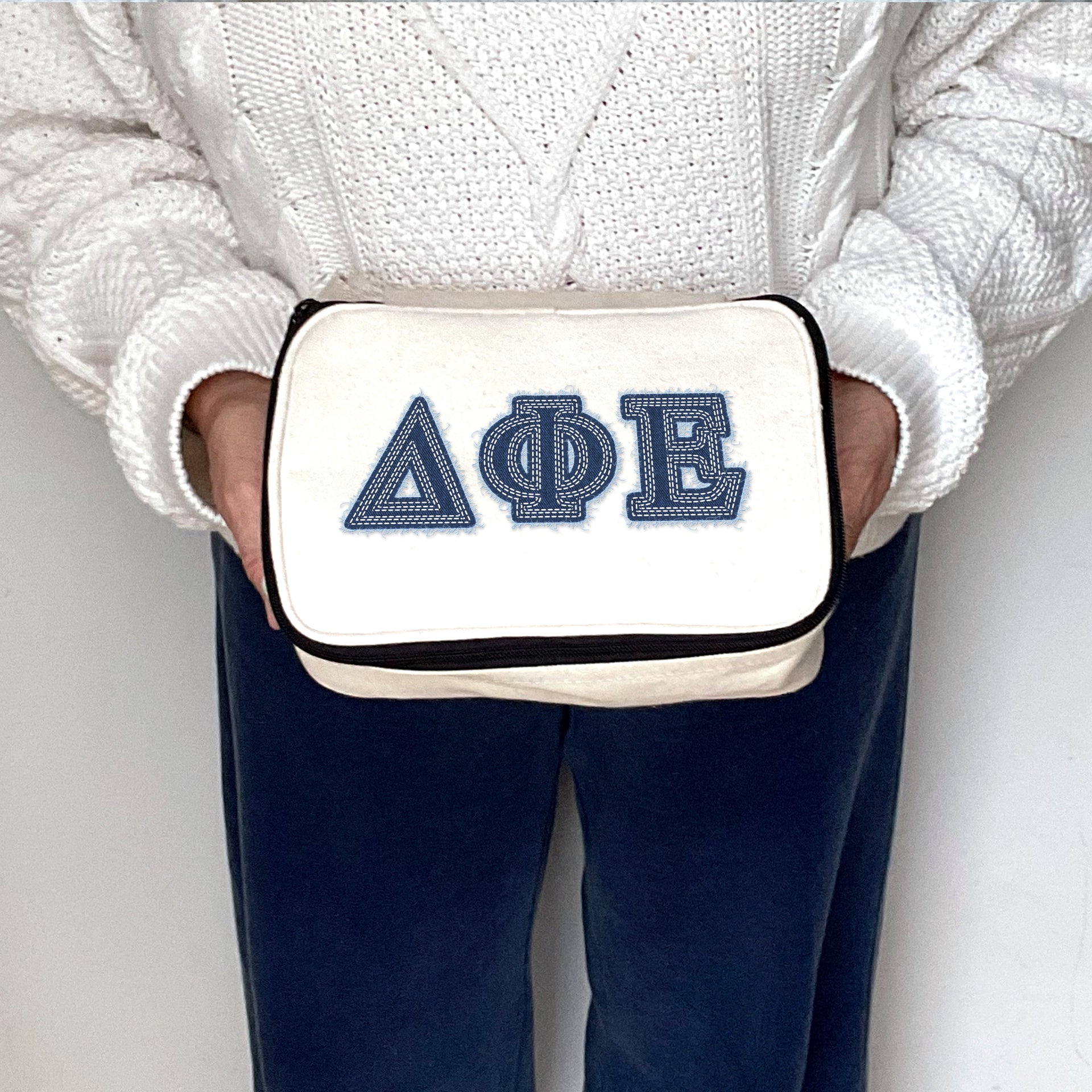 Delta Phi Epsilon makeup bag held and displayed with denim-inspired printed Greek letters.