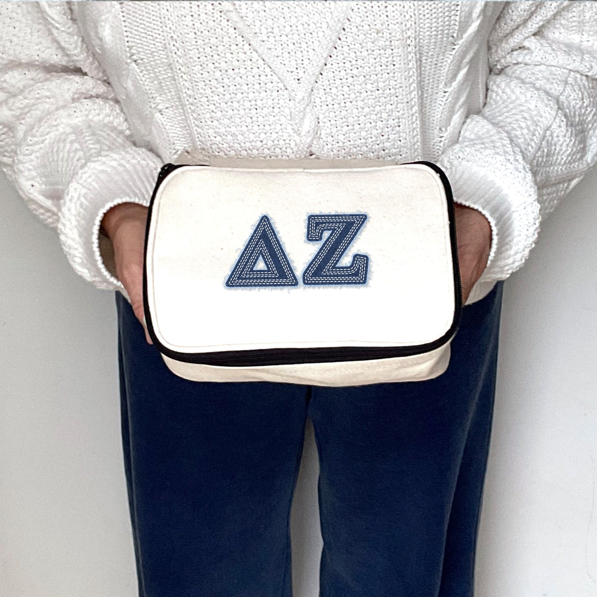 Delta Zeta canvas makeup bag printed with DZ denim-style Greek letters, held in hand.