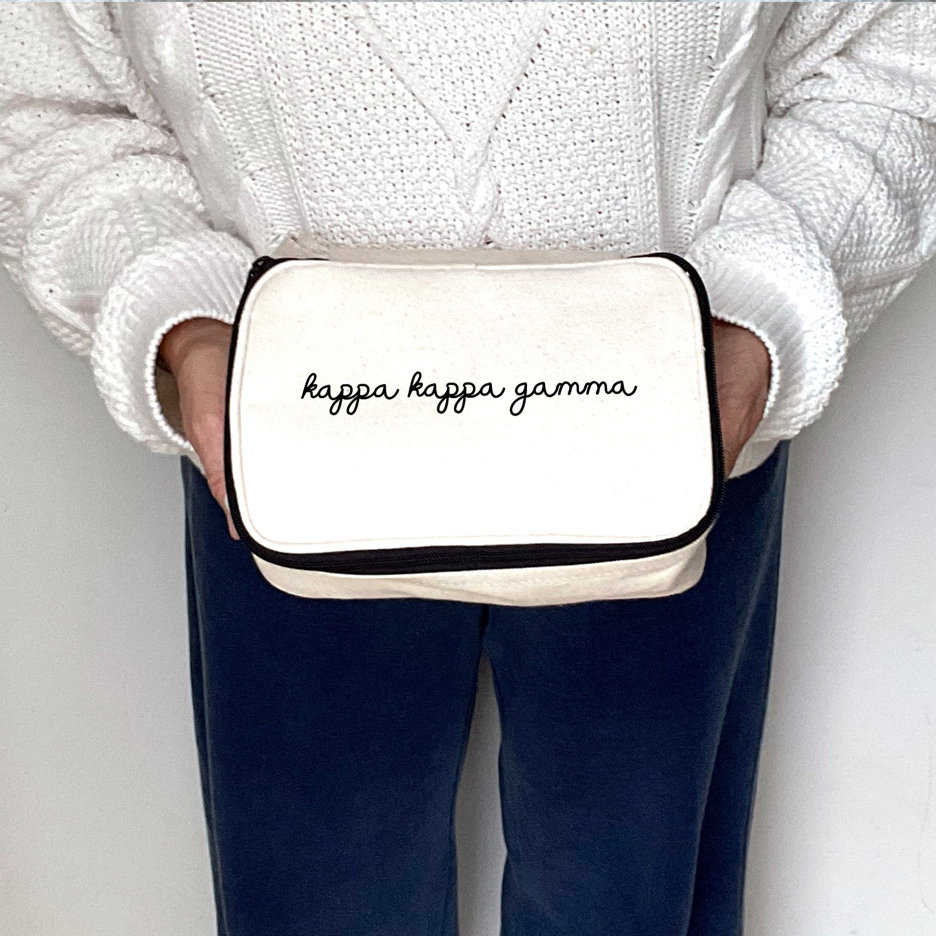 Mid-frame image of a woman holding a Kappa Kappa Gamma cosmetic bag with soft script lettering.