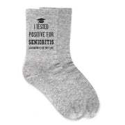 2024 Grad socks for the senior class of 2024 with I tested positive for seniorities graduation is the only cure digitally printed on the side of cotton crew socks.
