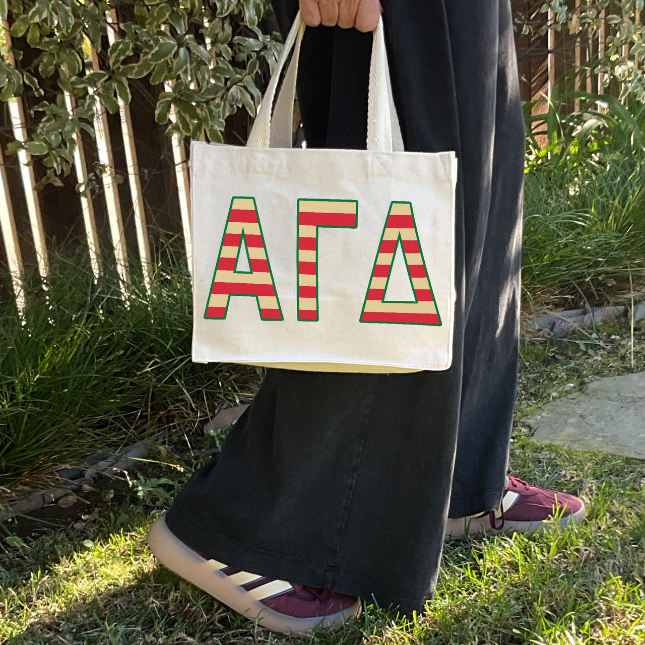 Model carrying the Alpha Gamma Delta Greek letters in sorority colors small striped tote.