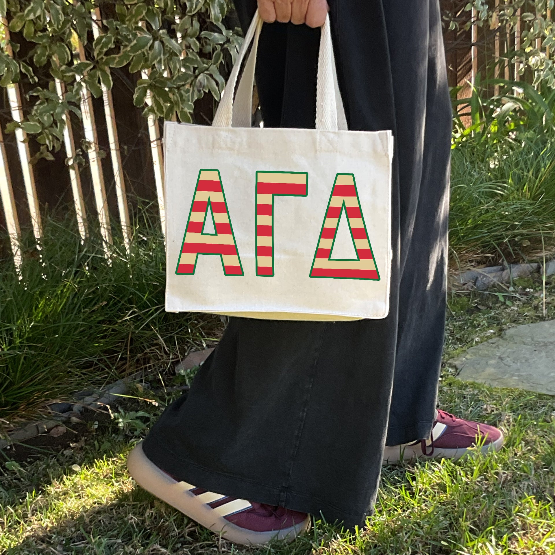 Model carrying the Alpha Gamma Delta Greek letters in sorority colors small striped tote.