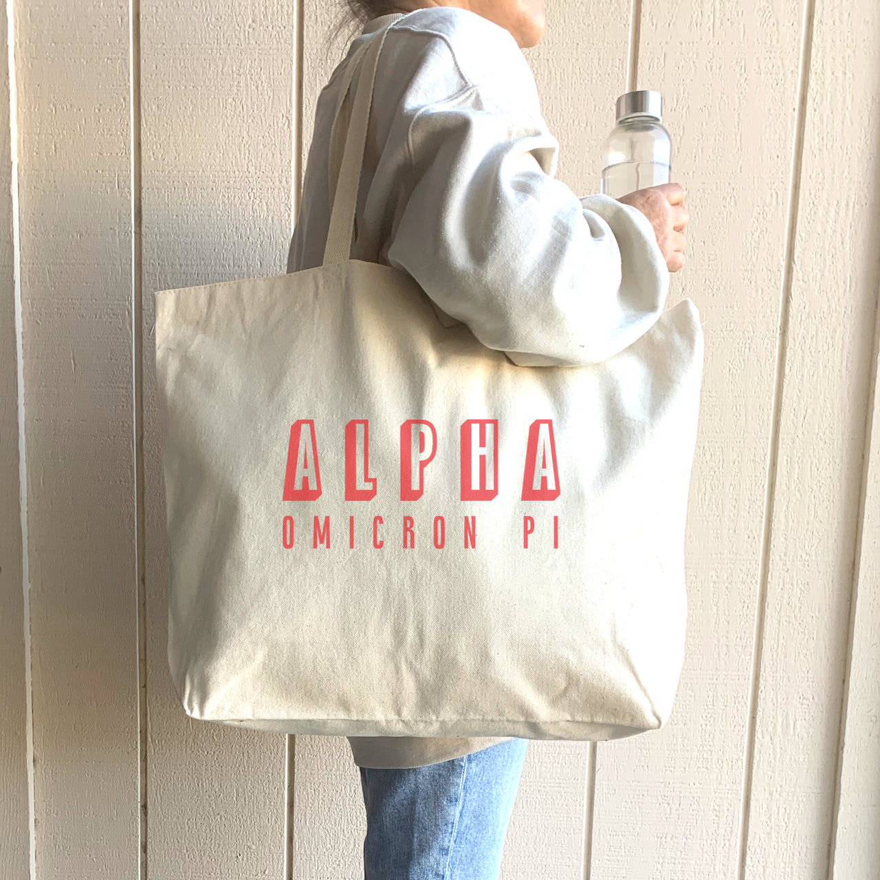 Alpha Omicron Pi sorority tote bag with standout raised lettering, worn on the shoulder by a sister on campus.