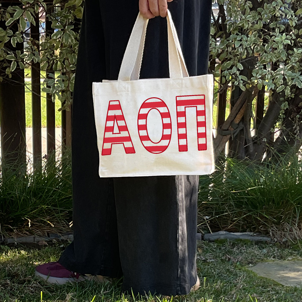 Model carrying the Alpha Omicron Pi Greek letters in sorority colors small striped tote.
