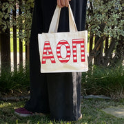 Model carrying the Alpha Omicron Pi Greek letters in sorority colors small striped tote.