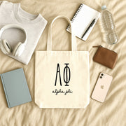 Alpha Phi small canvas tote bag with striped Greek letters styled in a flat lay with everyday essentials