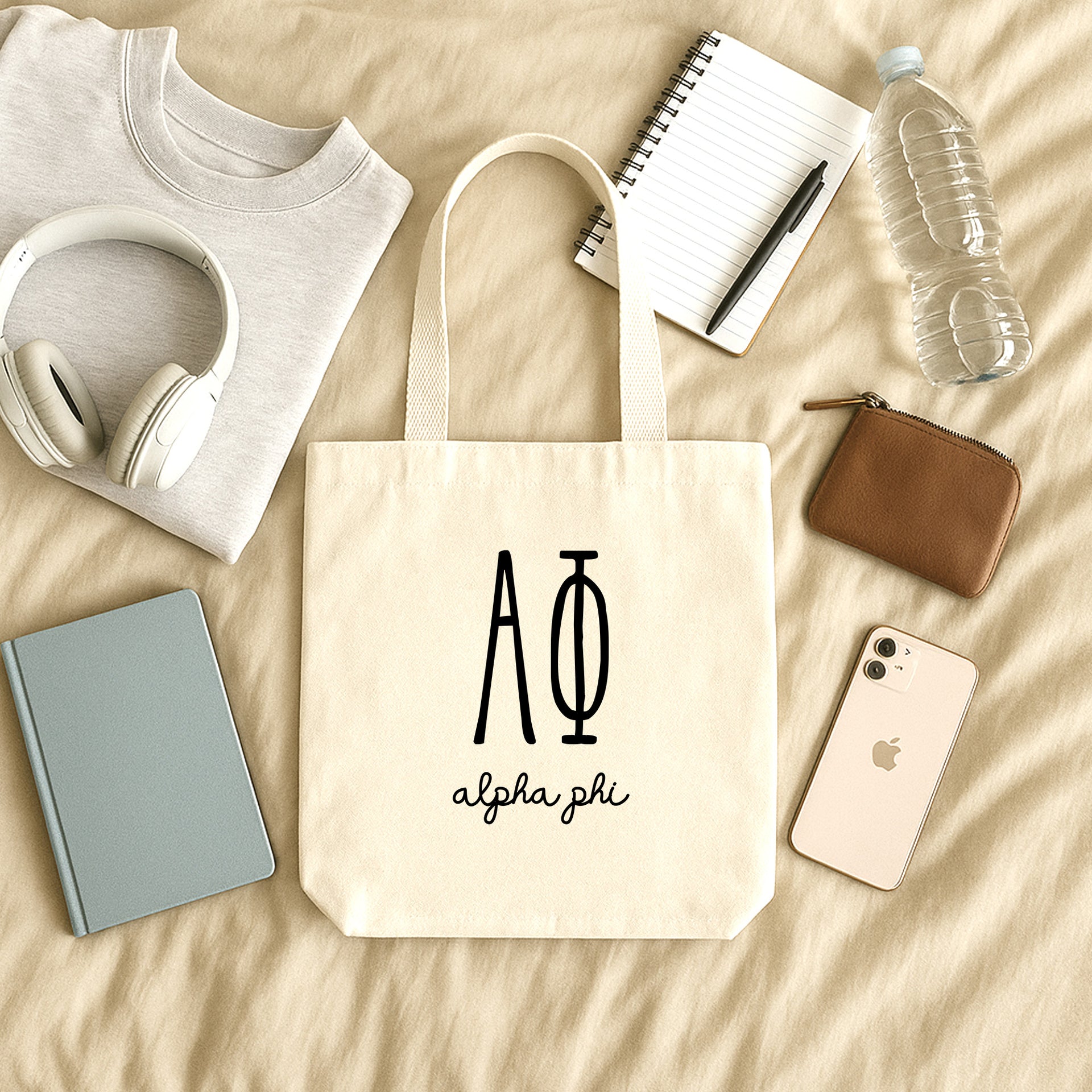 Alpha Phi small canvas tote bag with striped Greek letters styled in a flat lay with everyday essentials