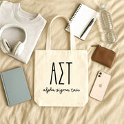 Alpha Sigma Tau small canvas tote bag with striped Greek letters styled in a flat lay with everyday essentials