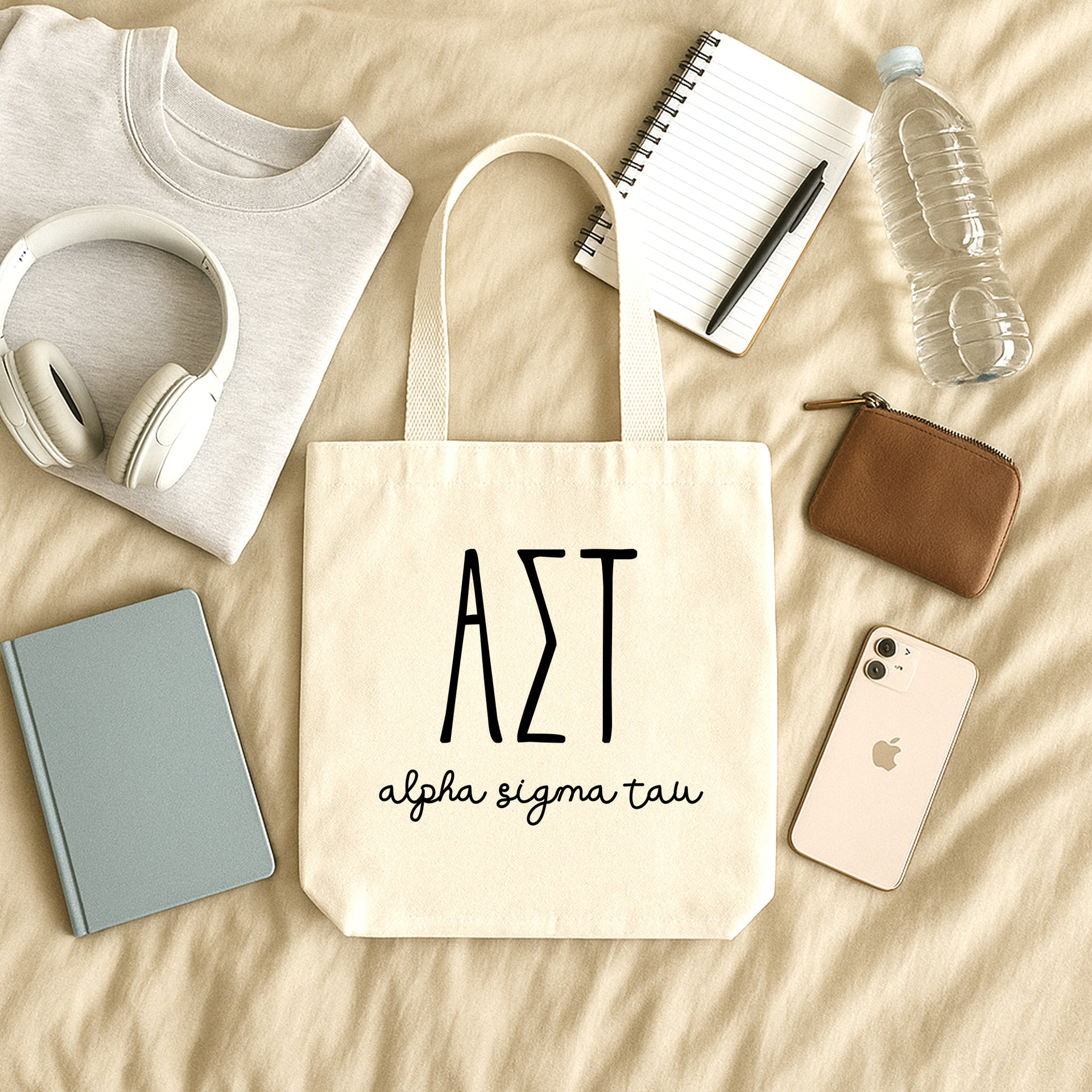Alpha Sigma Tau small canvas tote bag with striped Greek letters styled in a flat lay with everyday essentials