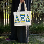Model carrying the Alpha Xi Delta Greek letters in sorority colors small striped tote.