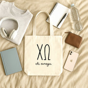 Chi Omega small canvas tote bag with striped Greek letters styled in a flat lay with everyday essentials