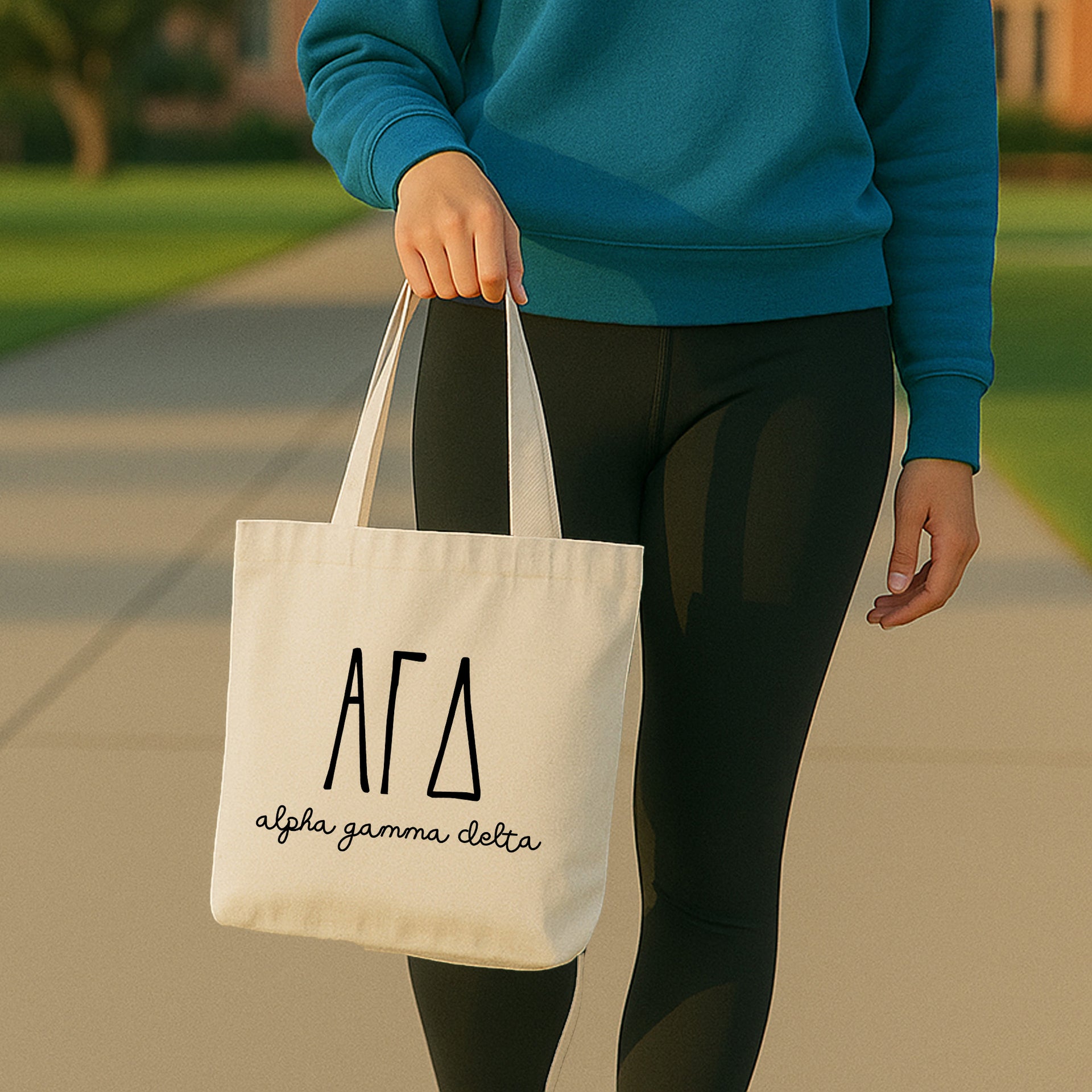 College student carrying an Alpha Gamma Delta small canvas tote bag with striped Greek letters