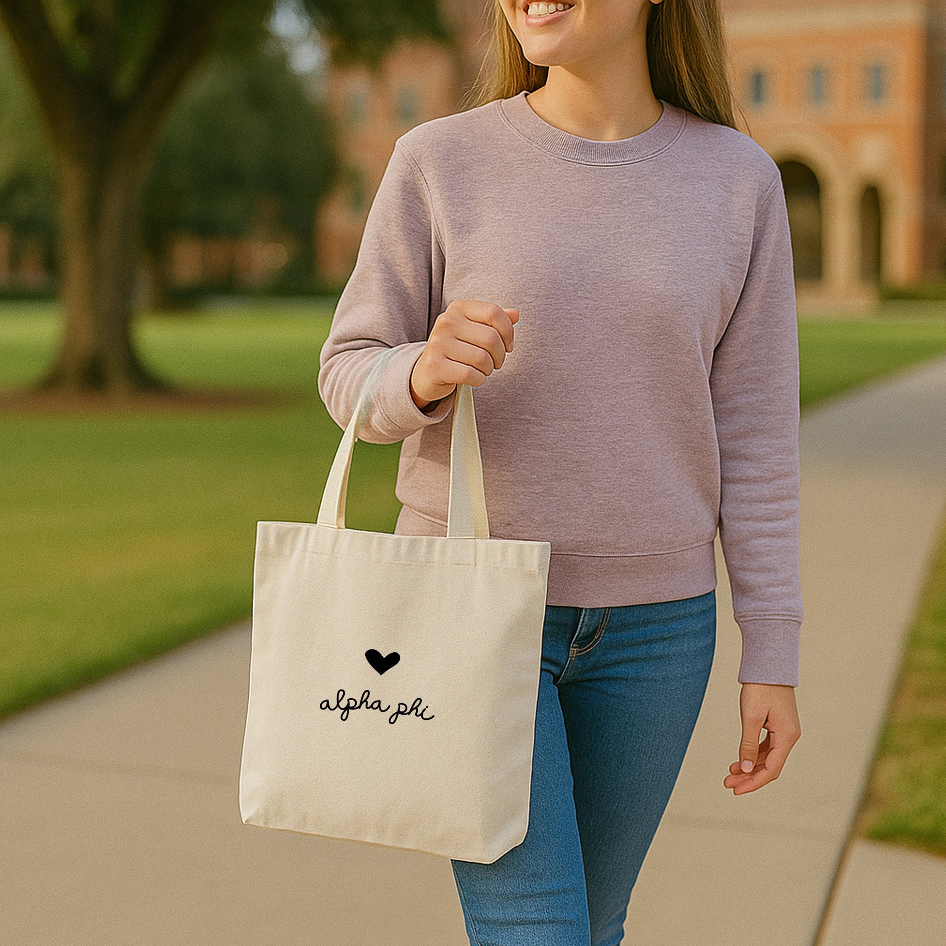 Alpha Phi small tote bag showing heart design with Alpha Phi Greek letters, carried at a university courtyard.