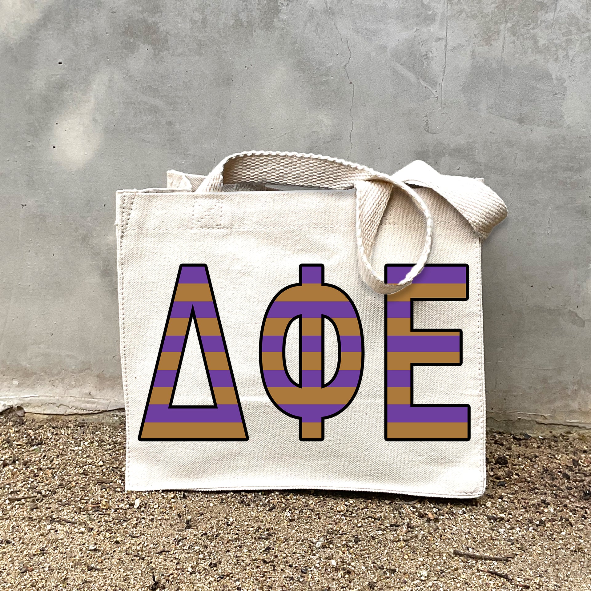 Model carrying the Delta Phi Epsilon Greek letters in sorority colors small striped tote.