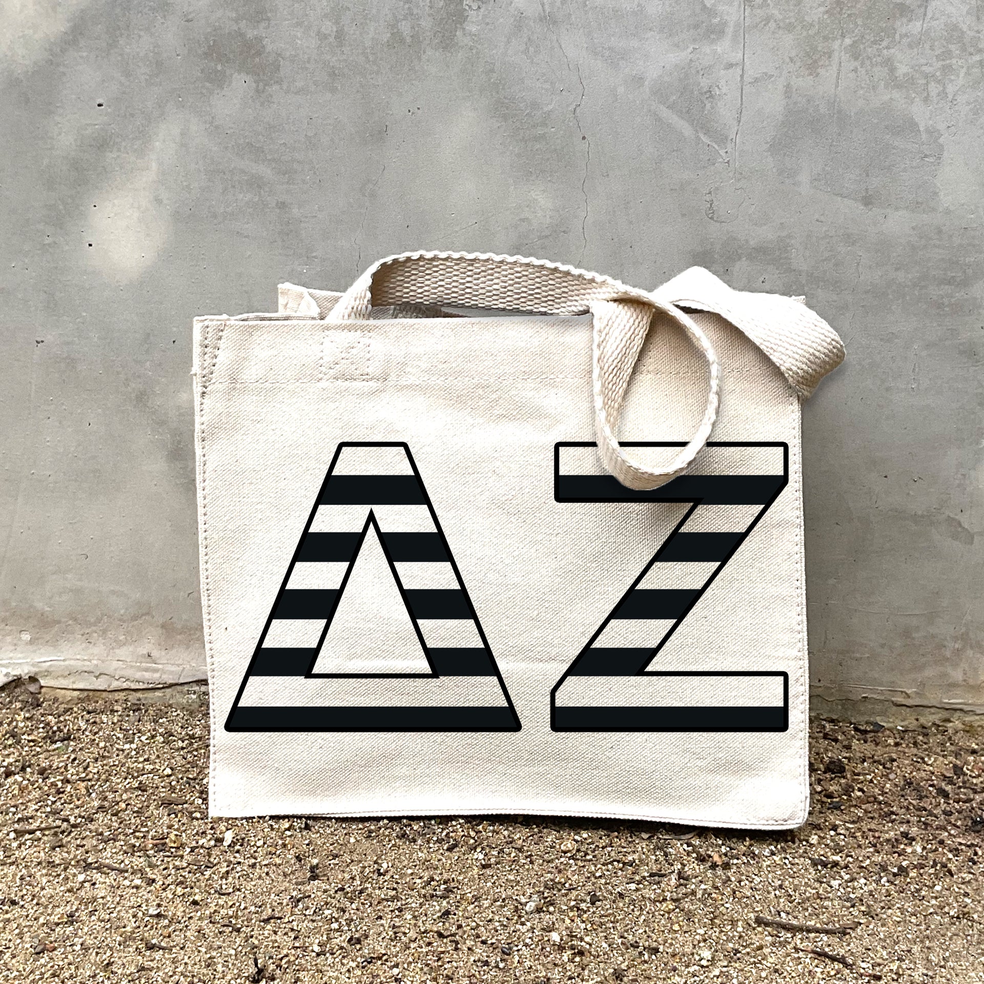 DZ Black Stripe In Black striped letters on a small canvas tote bag