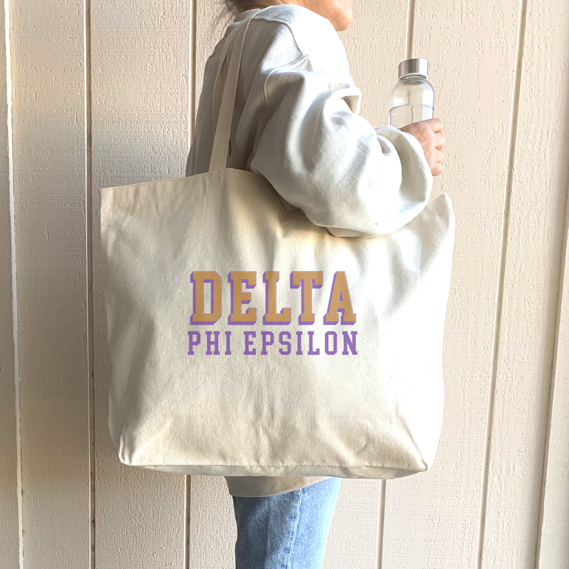 Delta Phi Epsilon sorority tote with standout 3D name, worn casually over the shoulder of a smiling sister.