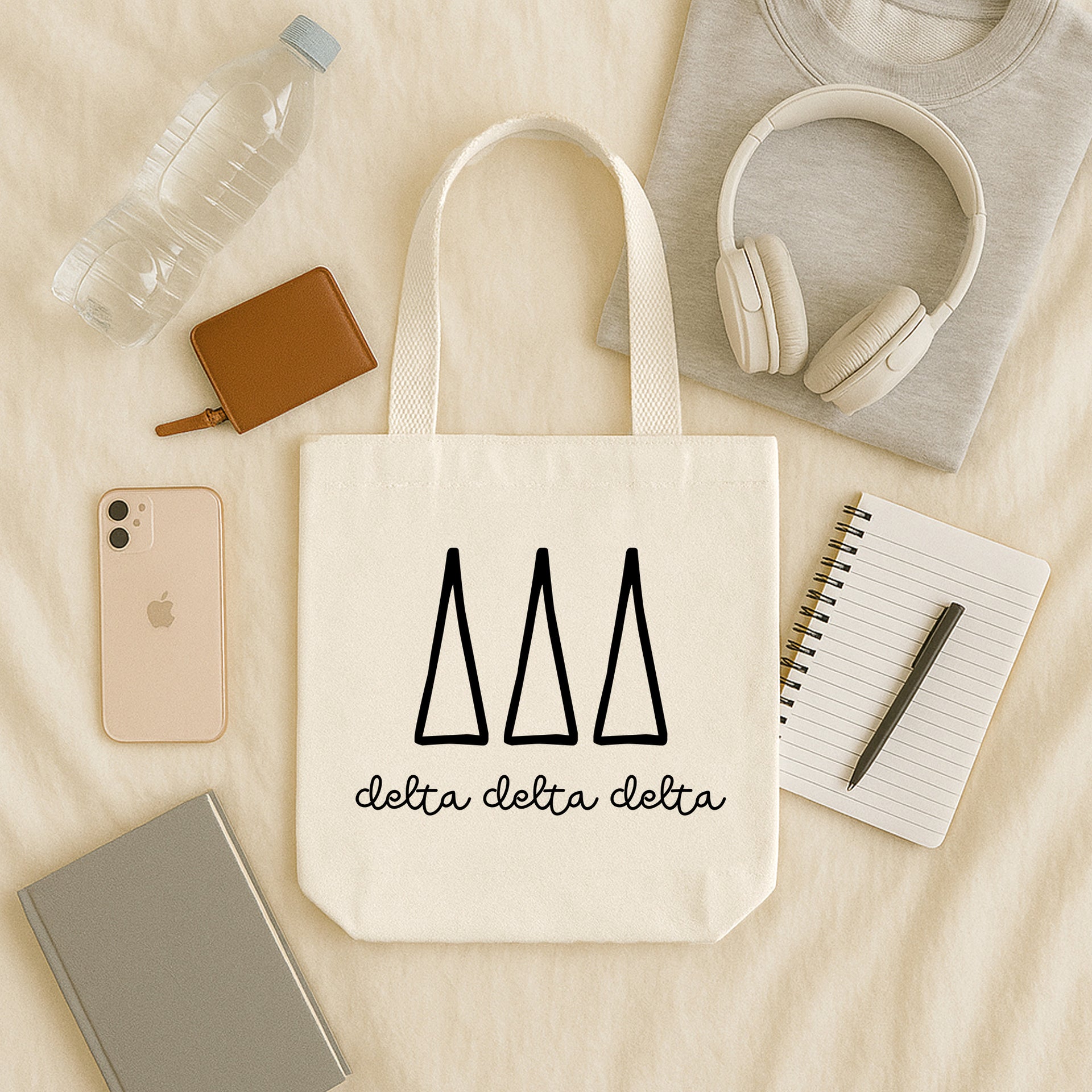 Delta Delta Delta small canvas tote bag with striped Greek letters styled in a flat lay with everyday essentials