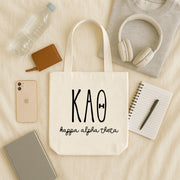 Kappa Alpha Theta small canvas tote bag with striped Greek letters styled in a flat lay with everyday essentials