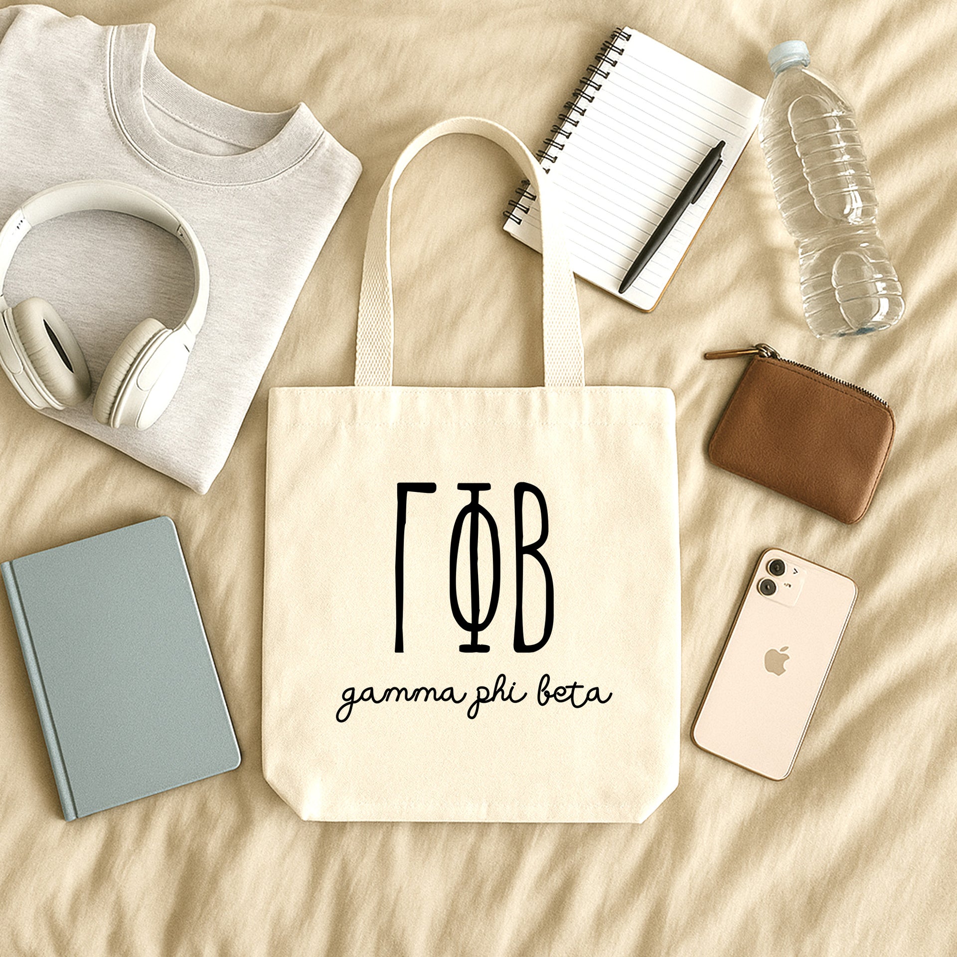 Gamma Phi Beta small canvas tote bag with striped Greek letters styled in a flat lay with everyday essentials