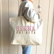 Gamma Phi Beta 3D design tote worn over the shoulder of a Gamma Phi woman in a cozy sweatshirt.