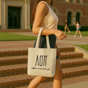 Alpha Omicron Pi woman carrying her small tote bag over her shoulder on a sunny day, printed with AOII Greek letters.