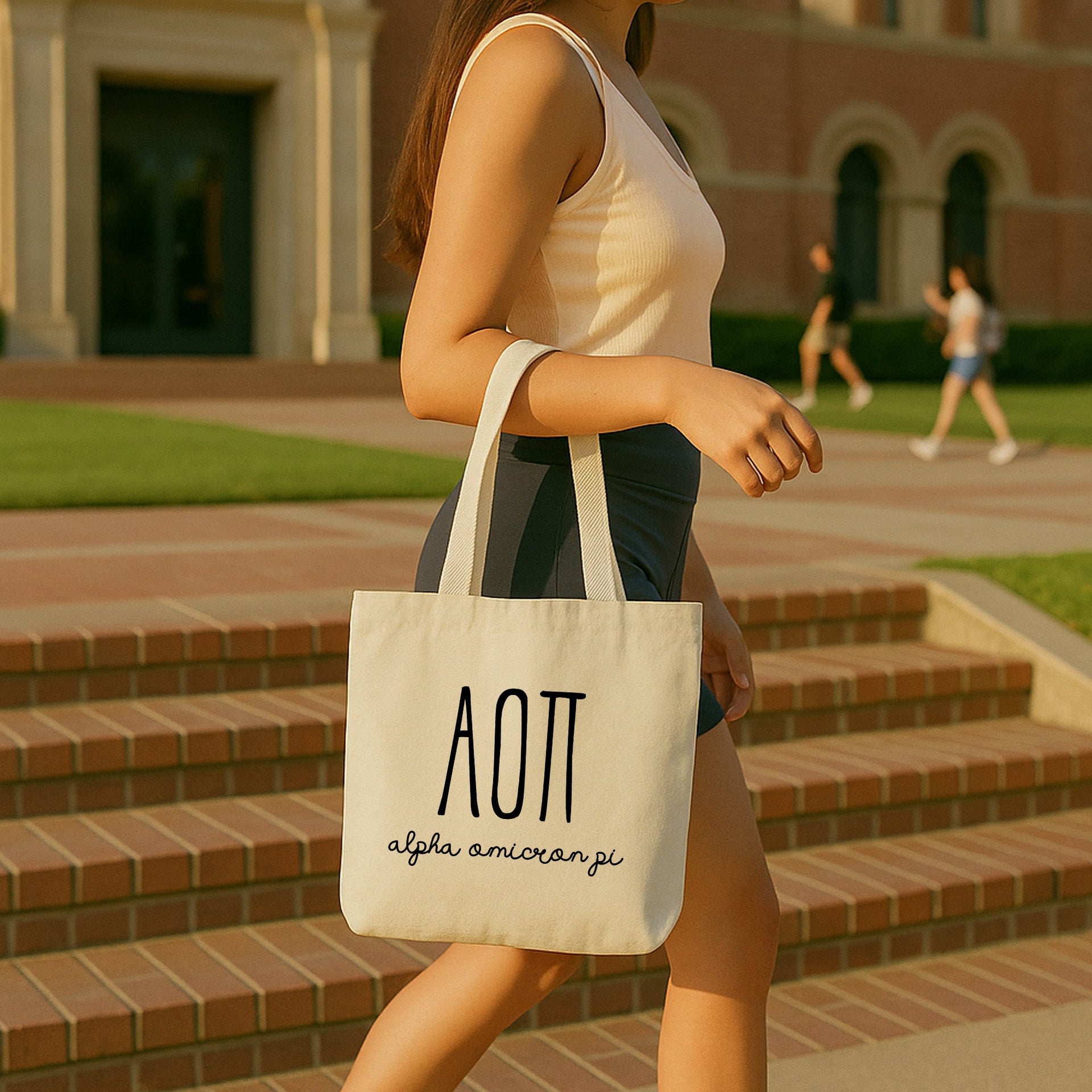 Alpha Omicron Pi woman carrying her small tote bag over her shoulder on a sunny day, printed with AOII Greek letters.