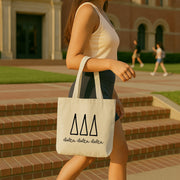 College student carrying a Delta Delta Delta small canvas tote bag with striped Greek letters