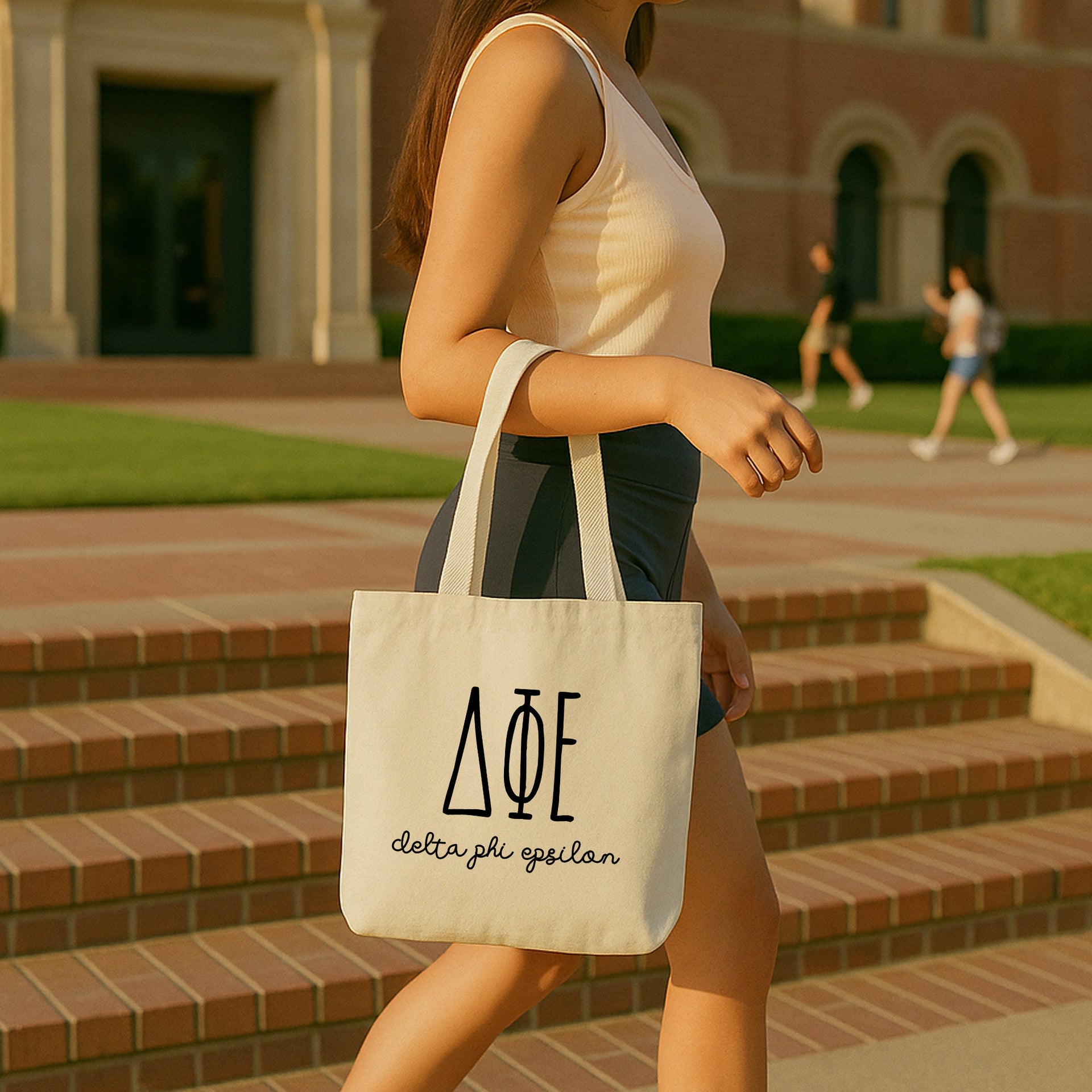 College student carrying a Delta Phi Epsilon small canvas tote bag with striped Greek letters